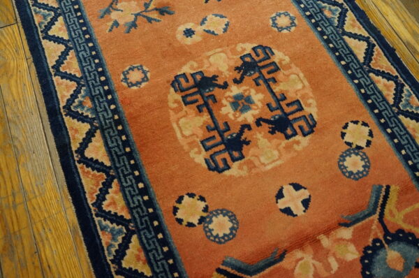 Coral rug with navy and light blue geometric borders and medallions rests on worn wood flooring.