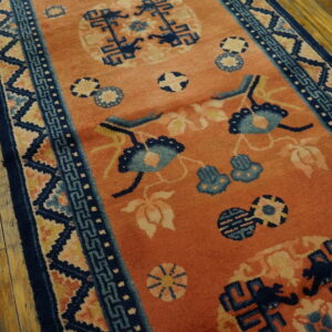An orange runner rug with navy and light blue traditional motifs is displayed on worn wood flooring.