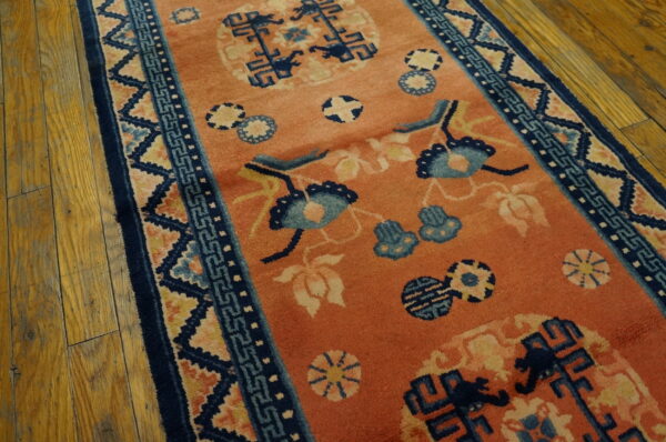 An orange runner rug with navy and light blue traditional motifs is displayed on worn wood flooring.