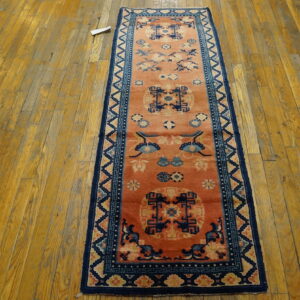A narrow runner with a rust-orange field and blue patterns rests on worn wooden plank flooring.
