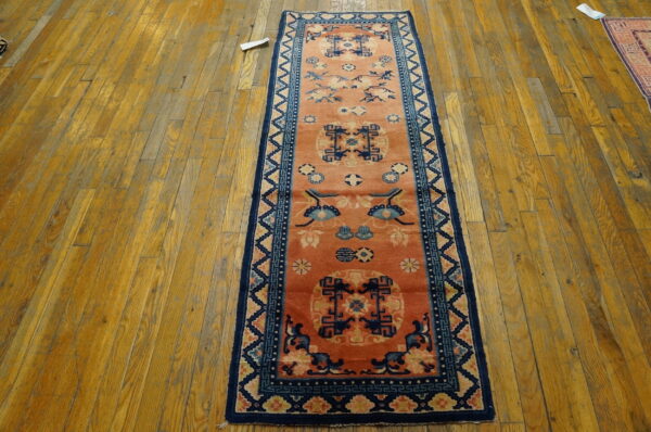 A narrow runner with a rust-orange field and blue patterns rests on worn wooden plank flooring.