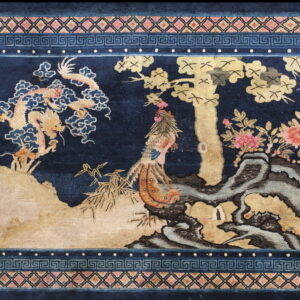 Deep blue rug with a gold, pink, and tan landscape design bordered by geometric patterns.