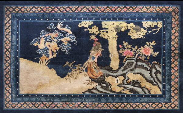 Deep blue rug with a gold, pink, and tan landscape design bordered by geometric patterns.