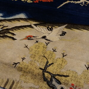 Textured rug detail of a white crane and yellow trees against deep blue and tan scenic background.