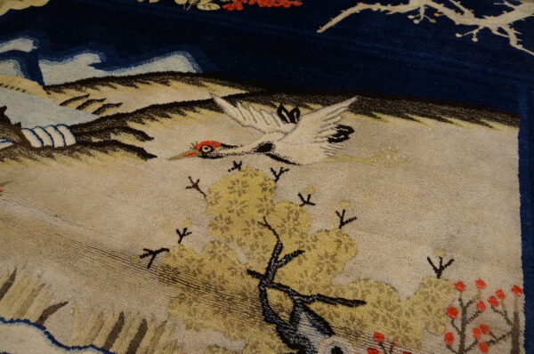 Textured rug detail of a white crane and yellow trees against deep blue and tan scenic background.