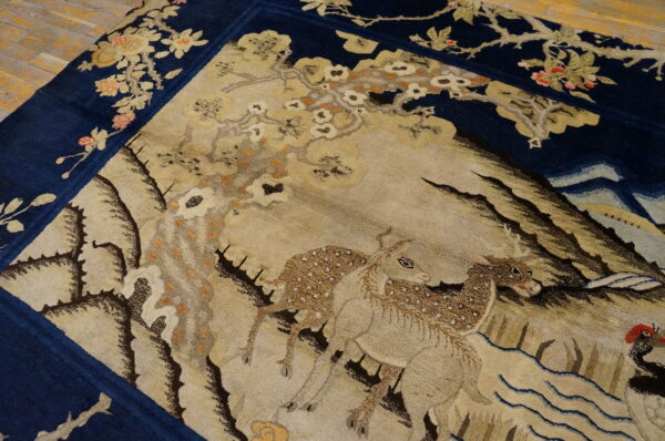 Navy and beige scenic rug featuring deer and flowering branches, displayed on light wood plank flooring.