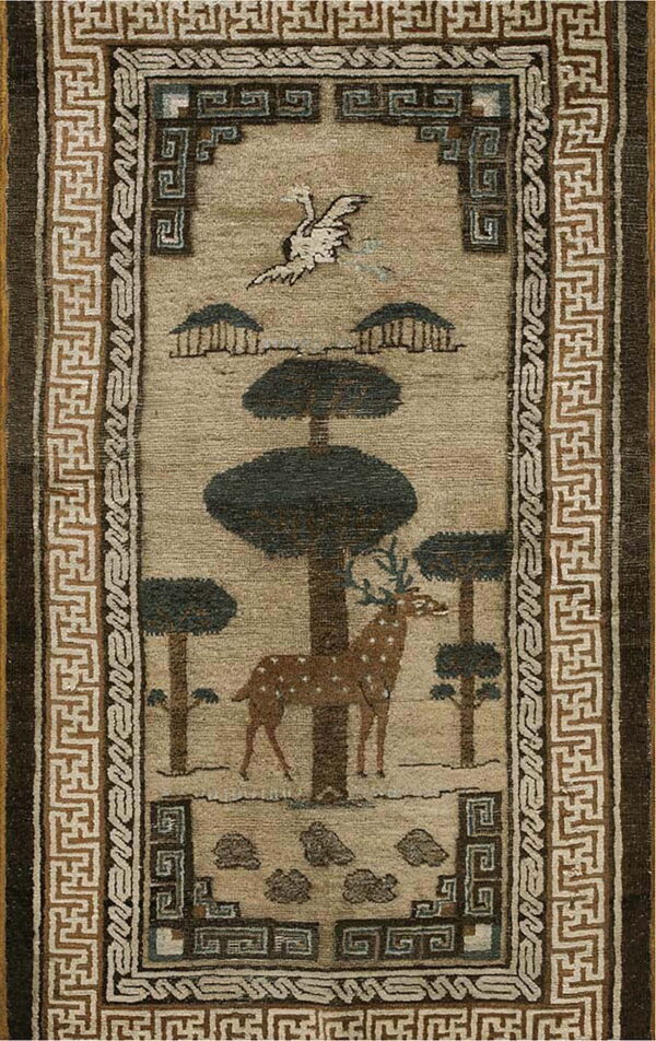 Tan rug with dark pictorial motifs of a deer and trees, bordered by brown and beige geometric fretwork.