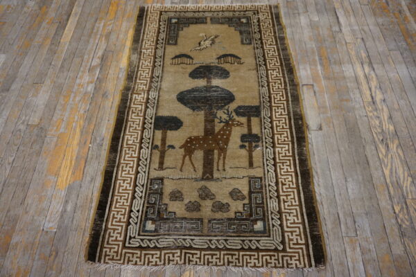 Tan runner rug with a brown deer and trees motif bordered by geometric patterns on weathered wooden planks.