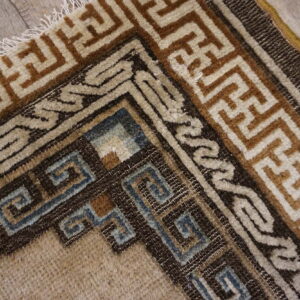 Geometric rug corner featuring beige, brown, and muted blue patterns on light plank wood flooring.
