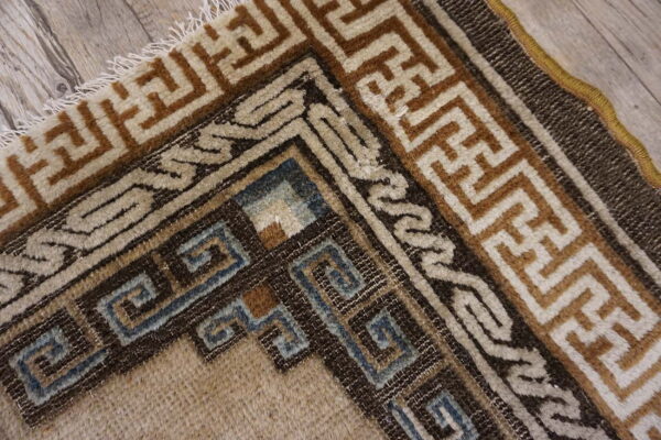 Geometric rug corner featuring beige, brown, and muted blue patterns on light plank wood flooring.