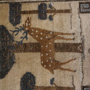 Tan and brown patterned rug with a spotted deer motif, bordered by meander and scroll designs.