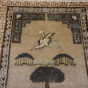 Tan rug featuring a stylized white bird and dark tree motif, framed by angular brown geometric borders.