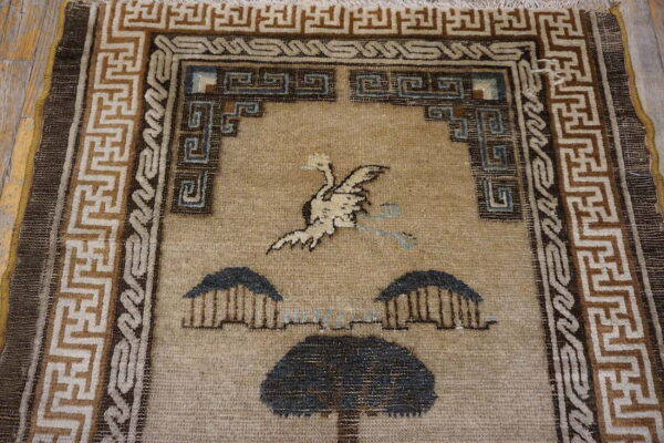 Tan rug featuring a stylized white bird and dark tree motif, framed by angular brown geometric borders.