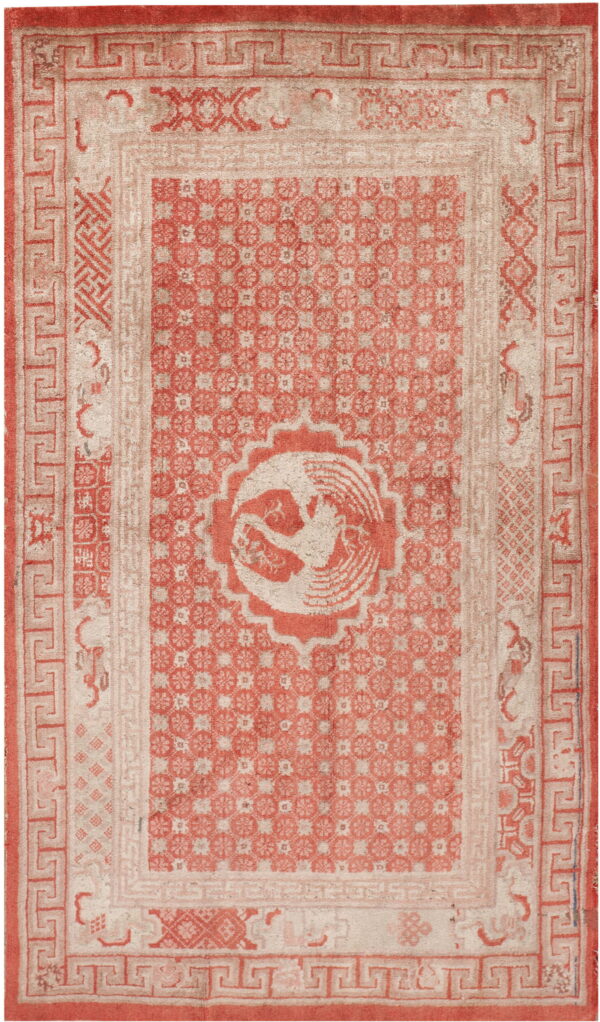 Distressed coral and beige rug with a complex greek key border and a central round bird design.