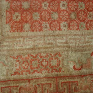Close-up of a high-pile rug featuring terracotta floral medallions and geometric borders on a taupe background.