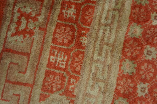 Textured close-up showing a faded rug pattern of terracotta blocks and geometric beige borders.