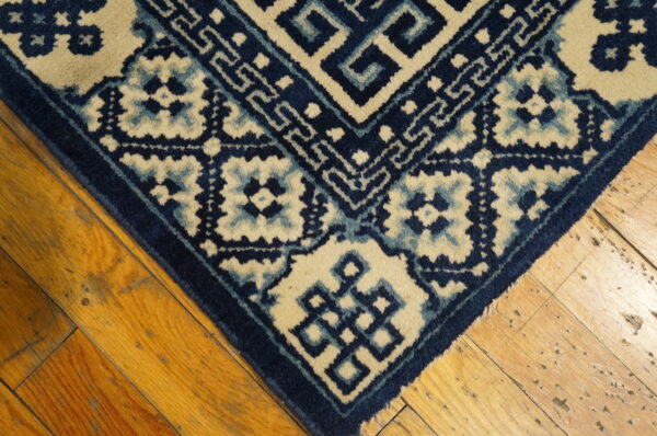 Navy, light blue, and cream rug with geometric and medallion patterns rests on distressed hardwood floors.