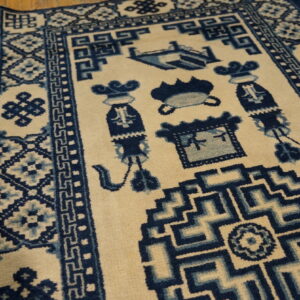 Detailed view of a cream rug with blue geometric borders and intricate symbolic center patterns on wood flooring.