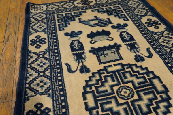 Detailed view of a cream rug with blue geometric borders and intricate symbolic center patterns on wood flooring.