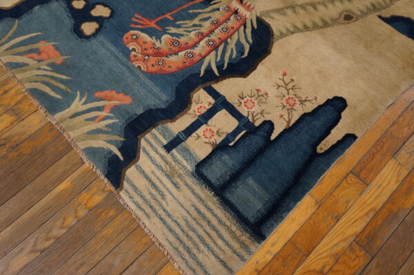 Small scenic pictorial antique chinese bird design baotou area rug 7 Detail of a blue and tan patterned rug with red and coral accents lying on distressed wood planks.