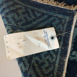 Coarse, deep blue and teal textured rug detail with geometric patterns and an attached white tag.