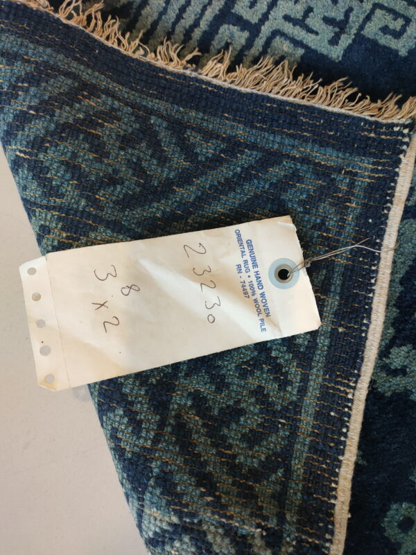 Coarse, deep blue and teal textured rug detail with geometric patterns and an attached white tag.