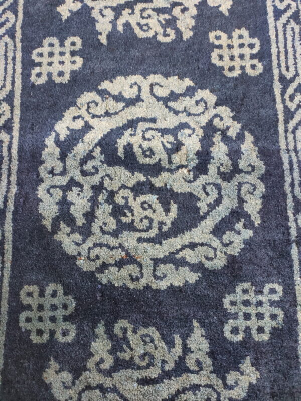 Dark blue high-pile rug featuring a circular traditional pattern and geometric motifs in faded light gray.