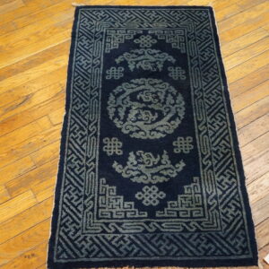 Navy and faded blue patterned mat rug with geometric borders sits on distressed light wood flooring.
