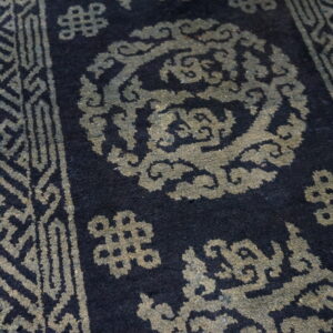 A close view of a dark blue rug with geometric and cloud patterns in muted greenish-gray on hardwood.