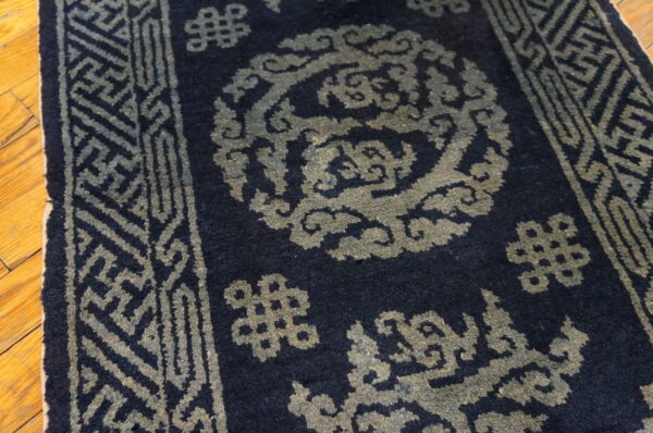 A close view of a dark blue rug with geometric and cloud patterns in muted greenish-gray on hardwood.