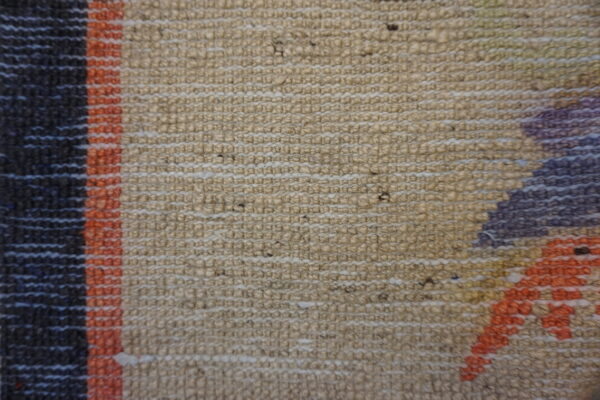 Knobby textured rug close-up featuring beige weave, dark stripes, and geometric patterns in orange and purple.