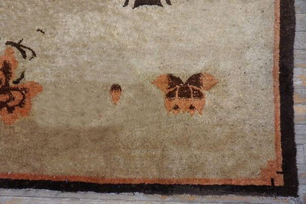 Textured tan rug with dark brown and burnt orange abstract patterns and a thick dark border.