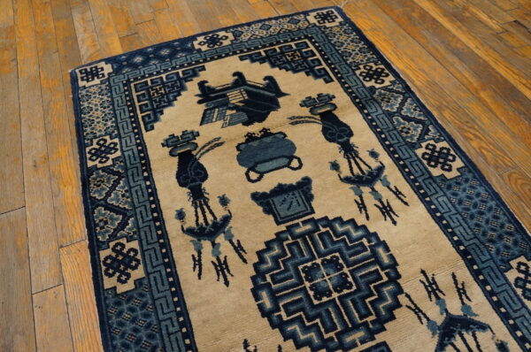 Tan and blue geometric patterned rug with stylized motifs on distressed plank hardwood flooring.