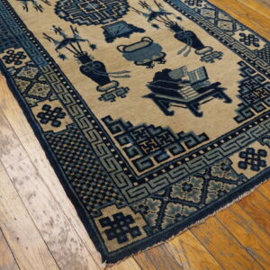 Traditional tan rug with elaborate blue motifs and geometric borders rests on worn plank wood flooring.