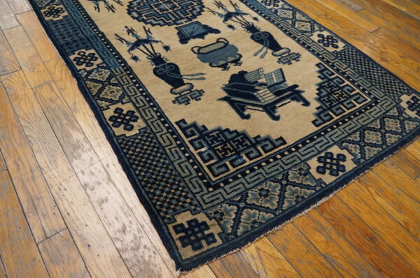 Traditional tan rug with elaborate blue motifs and geometric borders rests on worn plank wood flooring.