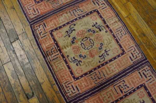 Geometric peach and purple rug runner with a pale green field lying on rustic wooden planks.
