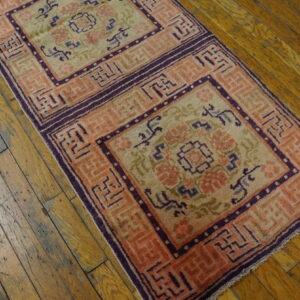 A runner rug with square medallions in peach, purple, and cream rests on worn wooden planks.