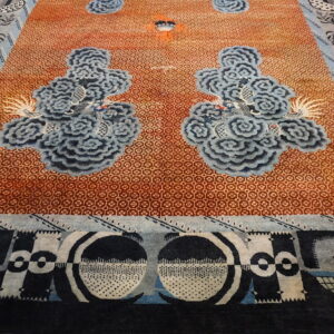 Orange rug with fine lattice work, large stylized blue cloud motifs, and abstract black and white borders.