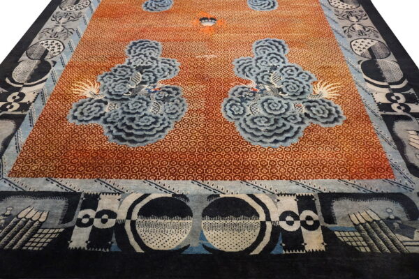 Orange rug with fine lattice work, large stylized blue cloud motifs, and abstract black and white borders.