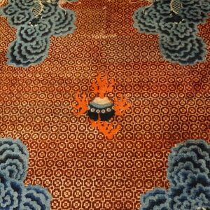 Geometric rust field featuring large sculpted blue cloud motifs and a central orange and black design.