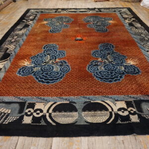 Rust-colored geometric rug with blue cloud patterns and complex black and gray borders displayed on wood flooring.