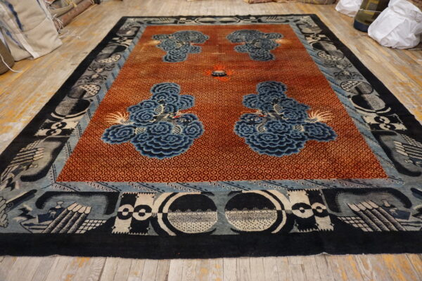 Rust-colored geometric rug with blue cloud patterns and complex black and gray borders displayed on wood flooring.
