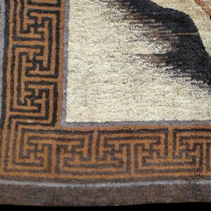 High-pile rug corner featuring a cream field, dark animal shape, and a brown geometric border.