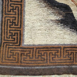 High-pile rug corner showing a beige field bordered by dark and medium brown key patterns.