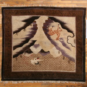 Pictorial rug featuring deer, birds, and mountains surrounded by a dark brown geometric border on wood.