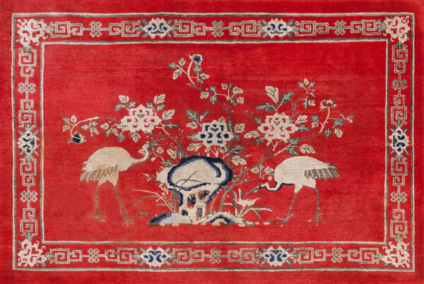 Traditional red rug with light beige and blue cranes, flowers, and a greek key patterned border.