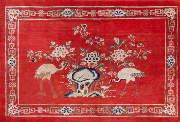 Red rug featuring white cranes and floral motifs, surrounded by a white and grey geometric border.