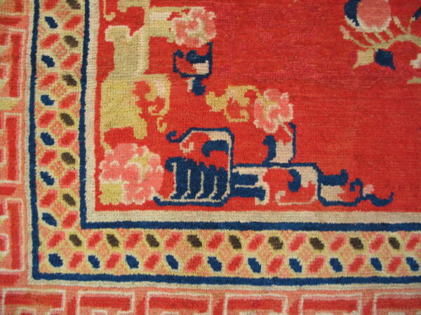 Detailed corner of a rug featuring red, blue, and yellow stylized floral patterns and geometric borders.