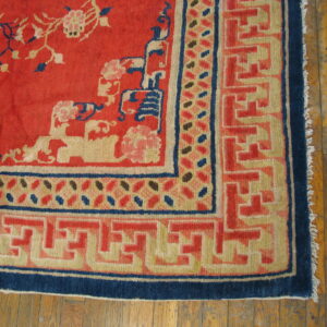 Red rug with scattered floral motifs and complex blue and tan geometric borders on distressed wood floor.