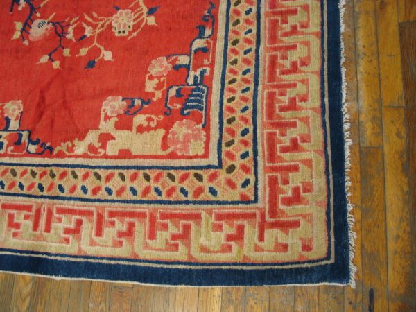 Red rug with scattered floral motifs and complex blue and tan geometric borders on distressed wood floor.